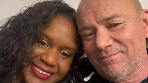 Supplied A selfie picture of Kacey a woman with black hair and Lee a man with short grey hair, smiling for the camera.