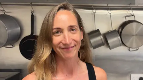 BBC Lady stood in a kitchen in front of pots and pans.