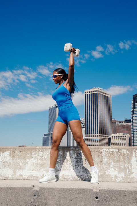 woman outside blue set lifting weights urban skyline