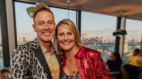 PA Media A middle-aged couple are in fancy dress at a party. They look happy.