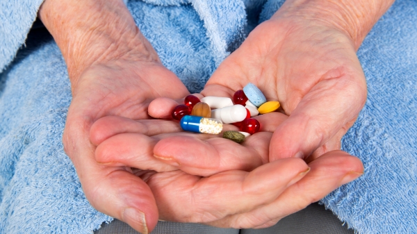 A person's hands holding half a dozen pills.