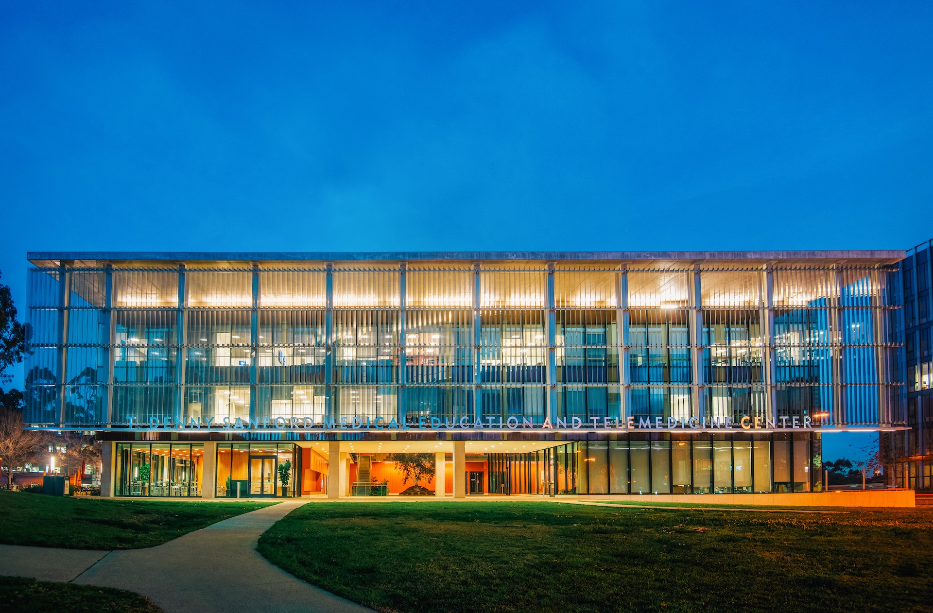 Photo of a four story building lit up at dusk with the words T. Denny Sanford Medical Education and Telemedicine Center