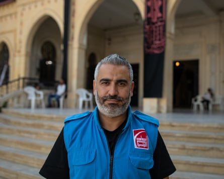 A bearded Middle Eastern man with grey-black hair wearing a blue paramedic uniform waistcoat
