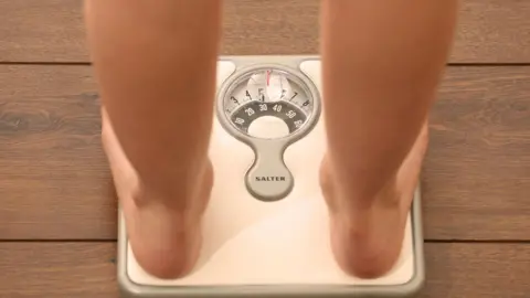 PA An image of someone using a set of weighing scales. Only part of their legs and feet are visible.