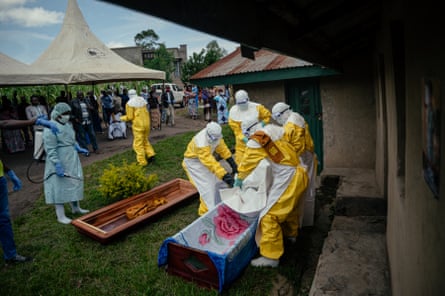 Members of a Congolese Red Cross team wearing protective clothing carry the body of a dead woman to place her in a coffin