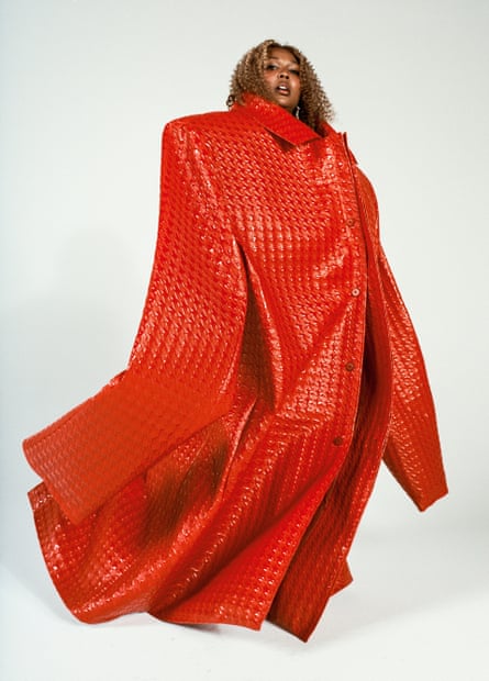Lizzo standing up, wearing a gigantic over-sized red coat