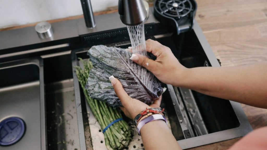 A woman washes raw leafy greens and asparagus in a sink to prevent cyclosporasis