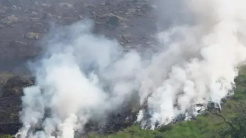 BBC Smoke can be seen billowing off moorlands after a fire quickly spread in the area. Patches of burnt grass be seen on the moorlands.