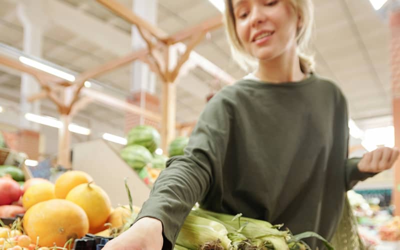 A woman reaches to grab a tomato from the grocery section in a supermarket.