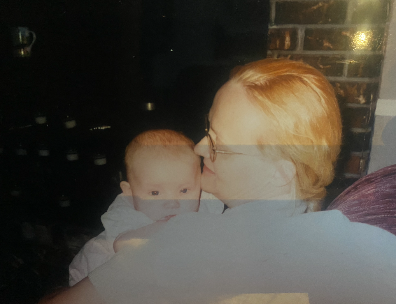 An adult holds a baby close, facing slightly turned away. The scene suggests a quiet, intimate moment