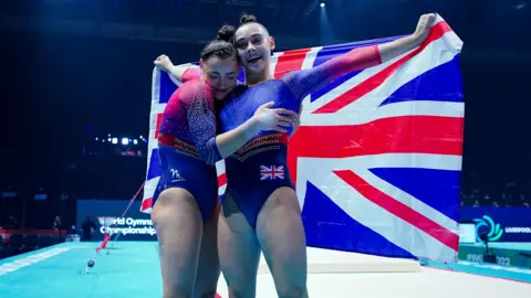 PA Media The Gadirova twins are dressed in red and blue leotards and holding the union jack behind them at the World Gymnastics Championship.