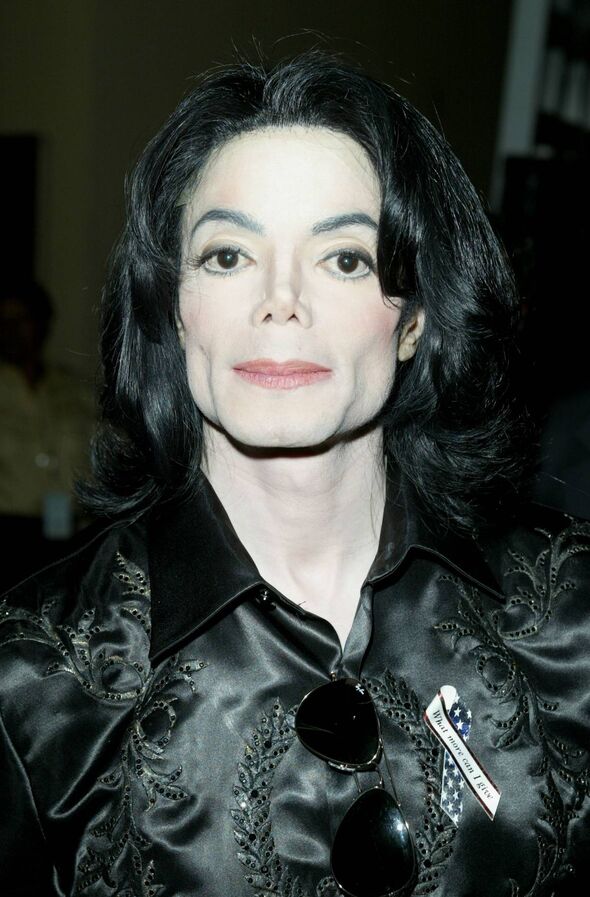 Alt Text: A close-up portrait of a person with short, straight black hair and distinctive facial features, set against a blurred