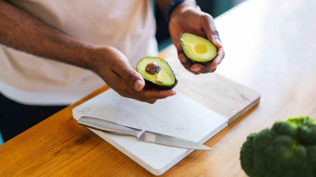 A person holding an avocado cut into two halves.