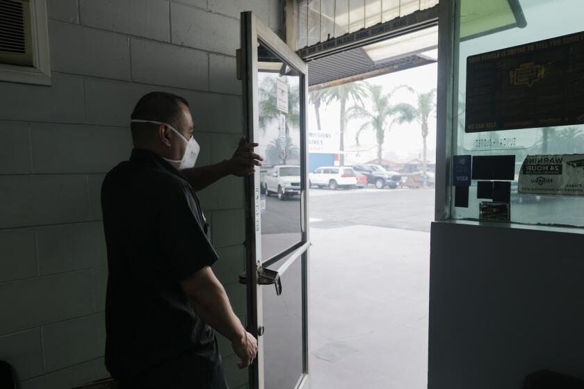 Los Angeles, CA - June 23, 2026: Manny Villasenor, whose father owns MV Automotive on East Olympic Boulevard, looks out the door at the smoke from the Lineage Logistics cold storage warehouse in Los Angeles, CA on Tuesday, June 23, 2026. Villasenor says that he's closed a bit earlier and put fans in the bays to help out the mechanics. One mechanic with asthma was told to stay home. (Myung J. Chun/Los Angeles Times)