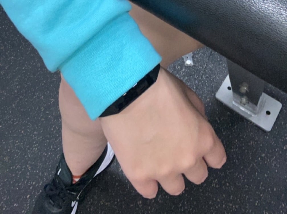 Person in a gym wearing a smartwatch and blue sweatshirt, resting arm on exercise equipment