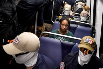 Members of Patriot Front ride the metro as a commuter looks on.