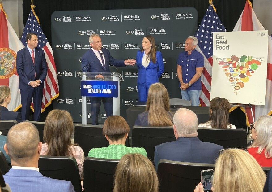 Four people surrounding a podium onstage. The podium says Make Hospital Food Healthy Again