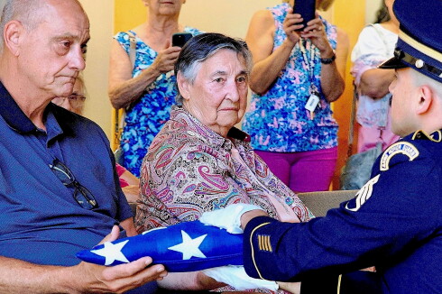 A man is presented an American flag by a solider during a funeral.
