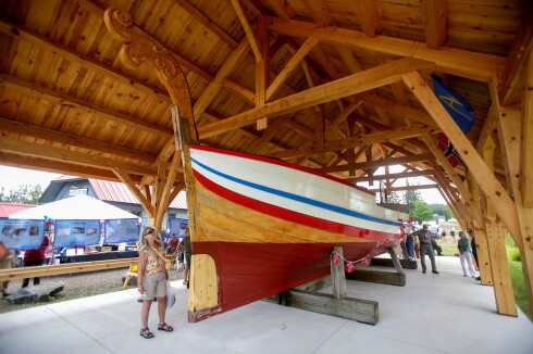 A woman looking up at a historic wooden ship displayed underneath a shelter at an outdoor center.