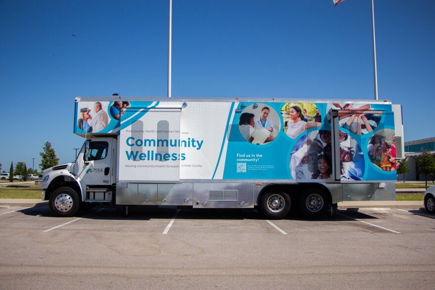 A blue-and-white mobile healthcare van is parked in a surface lot.
