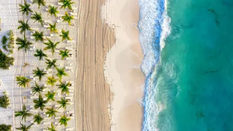Getty Images A beach in Cancun. The picture shows white sand, palm trees and an aqua sea with waves breaking on the shore
