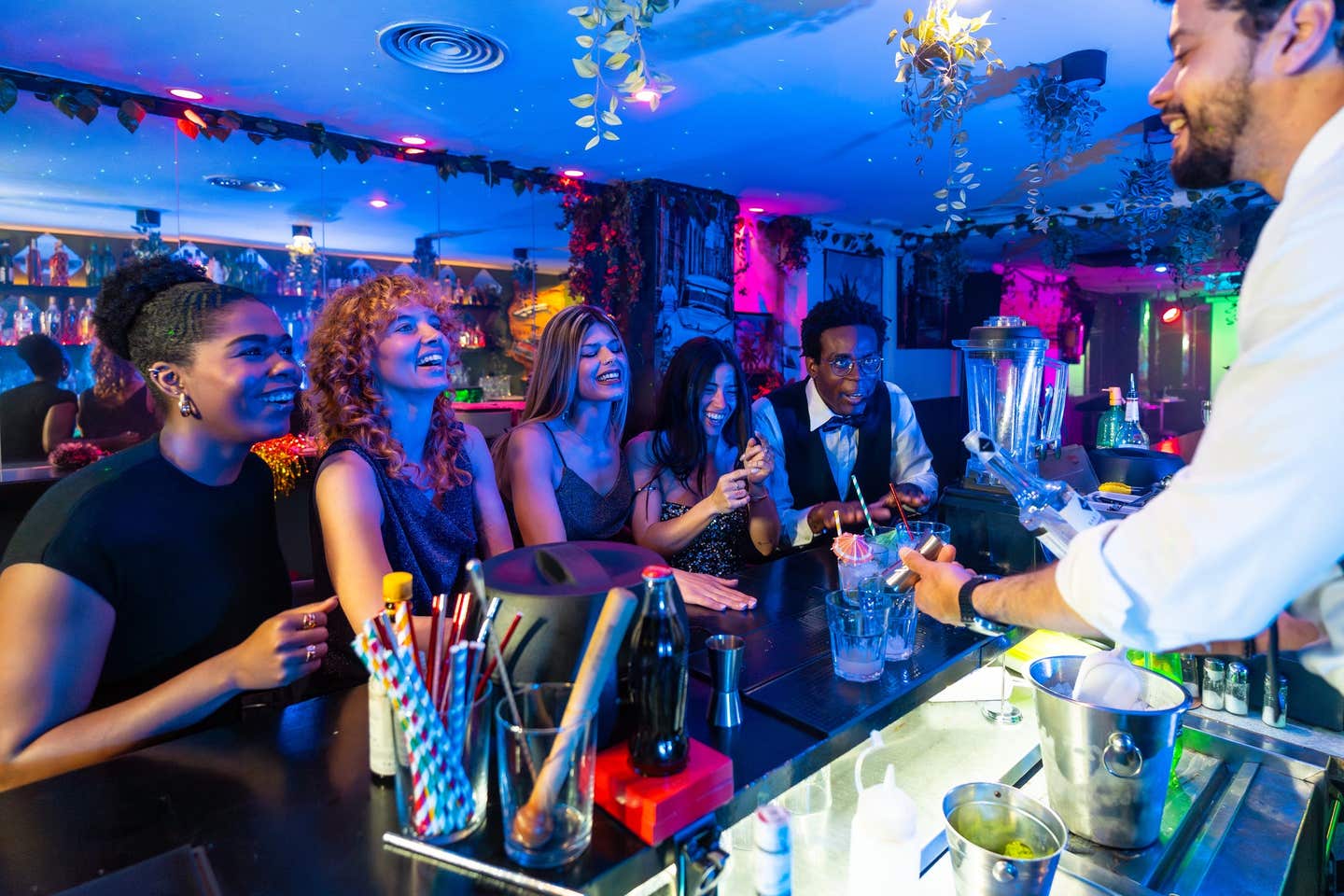 Group of friends ordering cocktails at the bar counter, talking and laughing with the bartender