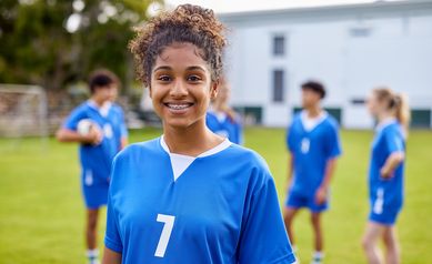 young female soccer player smiling at camera, a few teammates shown behind her