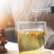 A person using a dropper to add liquid to a glass cup, possibly containing herbal tea or a supplement.