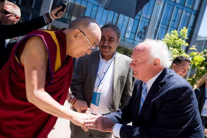 Dalai Lama in robes shakes hand of man, Denny Sanford, with Chancellor Khosla smiling in background