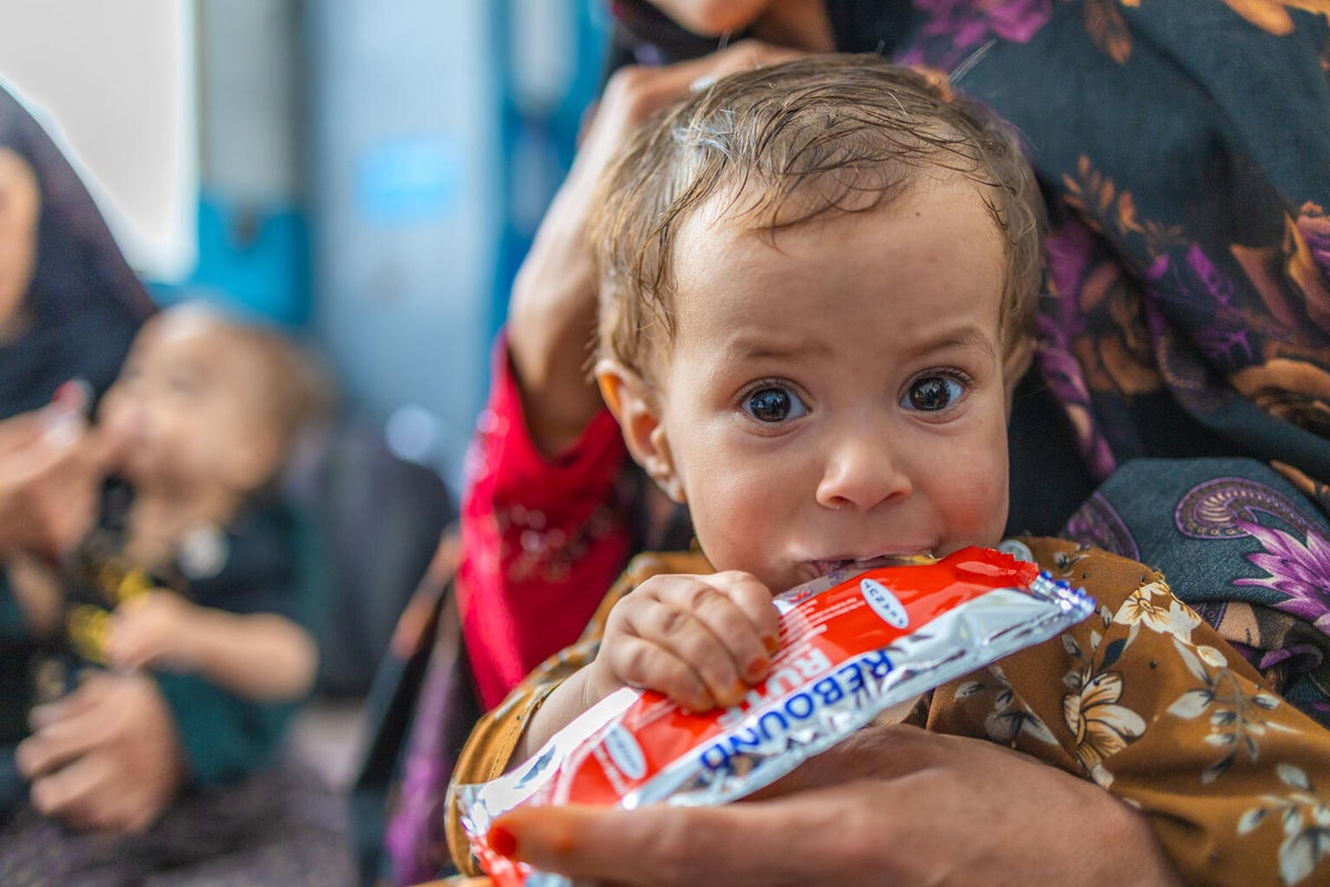 Baby sitting on mother's lap eating ready-to-use therapeutic food from a packet.