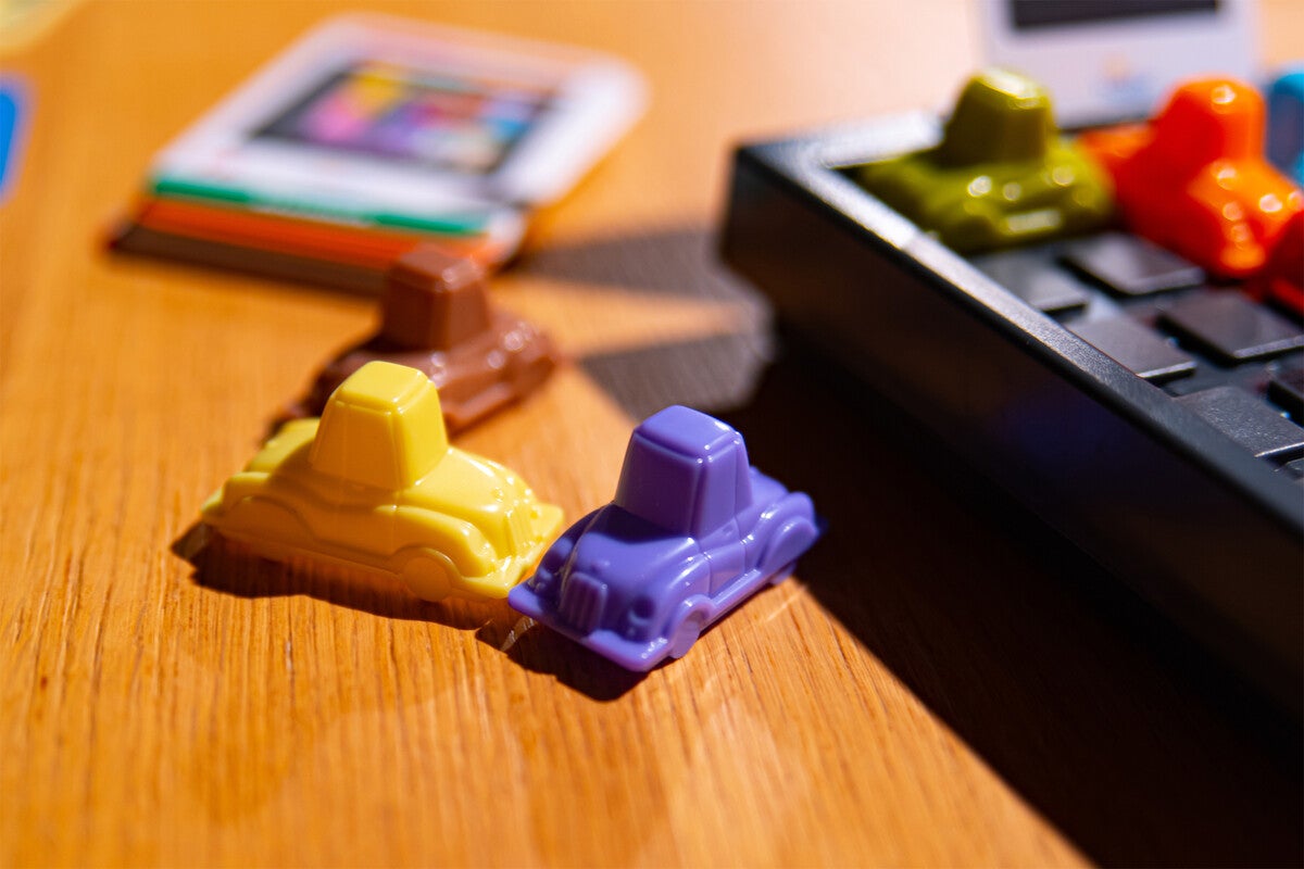 Three plastic cars from the puzzle game Rush Hour sit next to the puzzle board