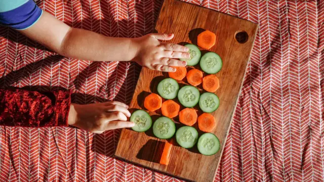 Hexagonal pieces of carrot and cucumber slices dey rest on a cutting board forming di shape of a pine tree.
