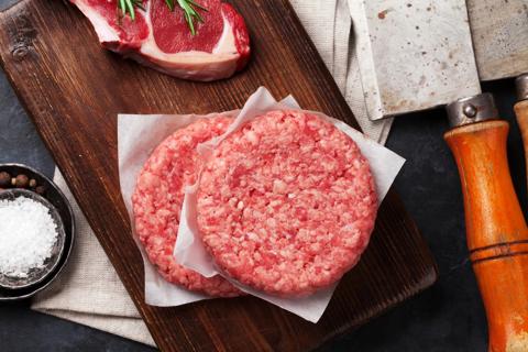 Two meat patties stacked on cutting board, with cut of lamb, salt and meat cleaver