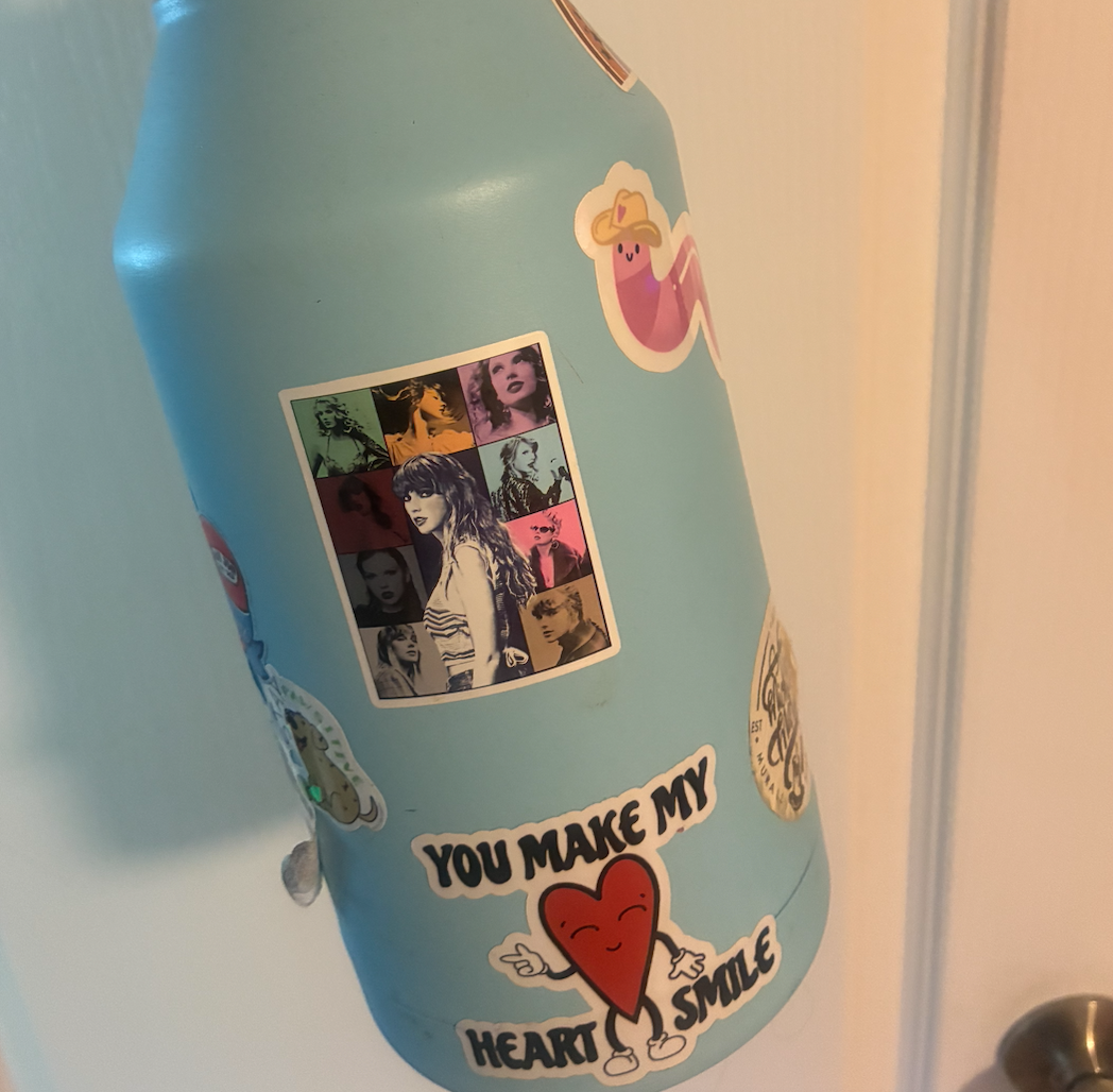Water bottle with colorful stickers, including cartoon characters and a pop art-style image of a woman. Text sticker reads, "You make my heart smile."