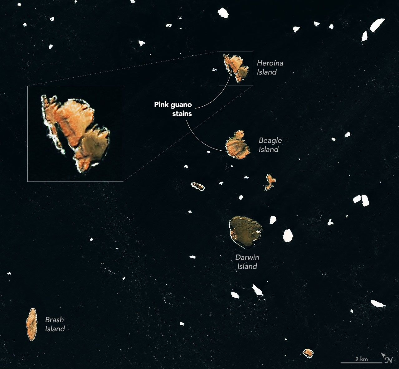 Several small islands, their surfaces tinged pink-orange, dot a dark ocean scattered with drifting sea ice.