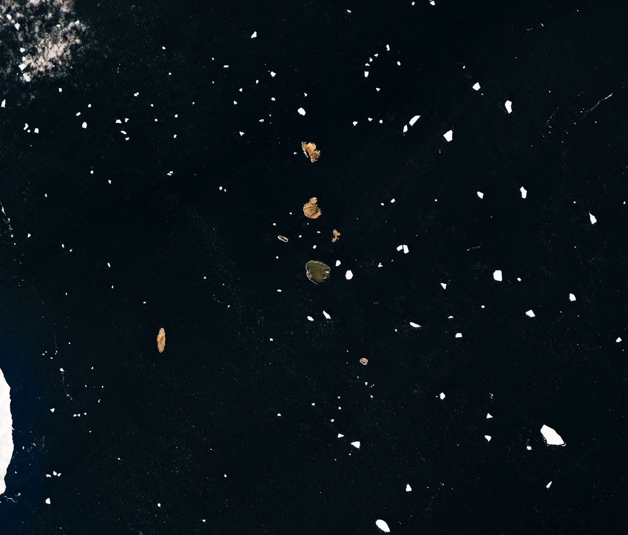 Several small islands, their surfaces tinged pink-orange, dot a dark ocean scattered with drifting sea ice.