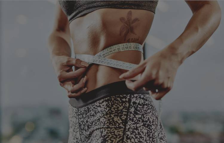 Close-up of a woman in workout clothes wrapping a measuring tape around her waist.
