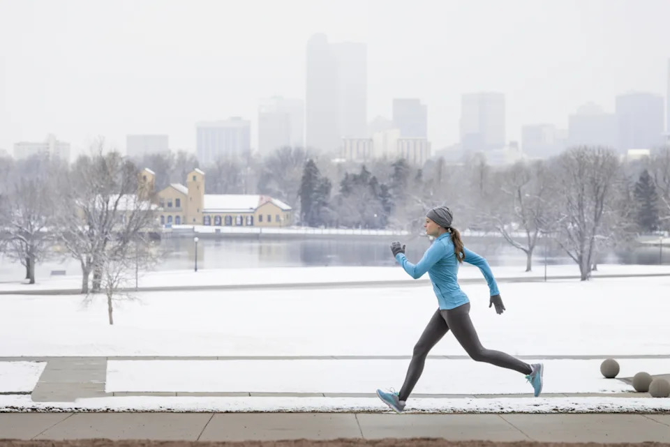 Runner running with a snowy landscape and Denver skyline in the backdrop.