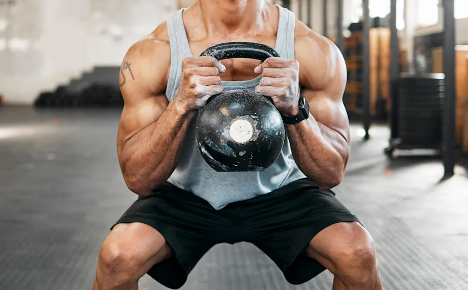 A person performs a goblet squat while holding a kettlebell in a gym.