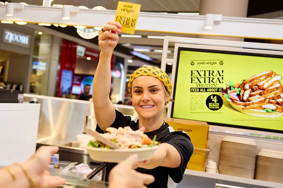 Footballer Ellie Carpenter behind the counter at Soul Origin giving out a chicken salad to a customer off camera
