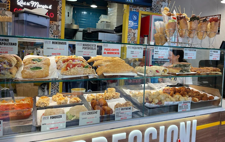 Food stall in Napoli with shelves stocked with sandwiches, pasta, bread, and fried foods