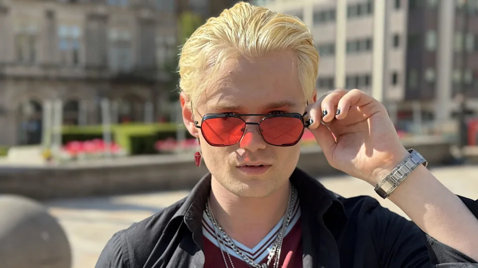 A close-up photo of a man with light blond hair, pink sunglasses, and an Aston Villa shirt.