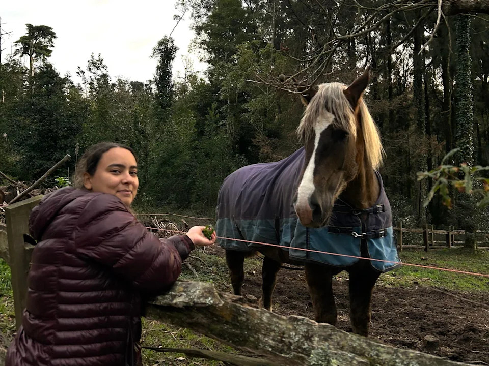 The writer wearing a puffer coat and standing near a horse in Sintra, Portugal.