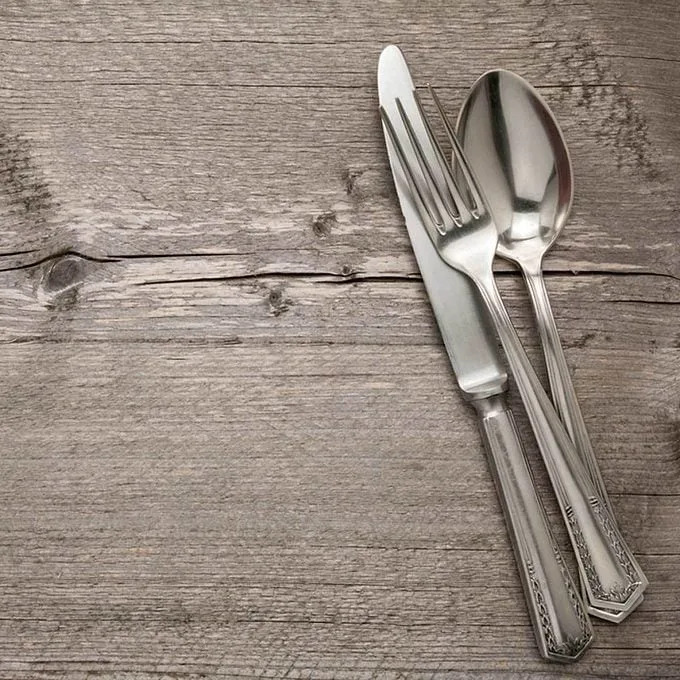 A knife, fork, and spoon are arranged neatly on a weathered wooden surface, suggesting readiness for dining or a meal setting.