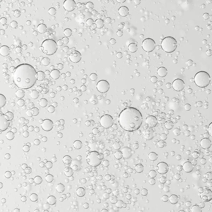 Clear bubbles float and rise in a transparent liquid, creating a lively, effervescent effect against a light background.