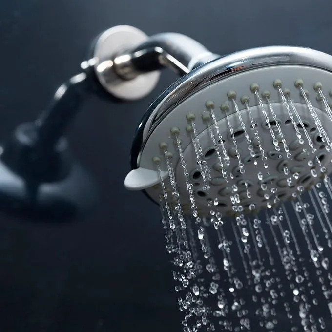 A showerhead releases a stream of water droplets, creating a refreshing cascade against a dark, sleek bathroom surface.