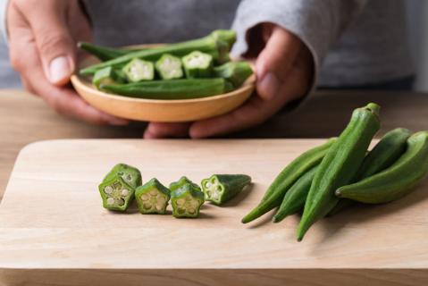 Hands holding bowl of okra, with sliced and whole okra on cutting board