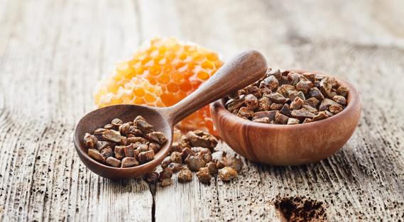 Chunks of bee propolis in wooden bowl and spoon, with honeycomb on table