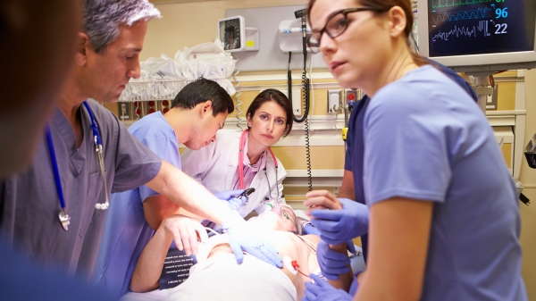 Image of health care professionals around a patient with an oxygen mask in a hospital room.
