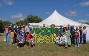 Group of Veggie Fest Chicago organizers and volunteers posing in front of a large “Veggie Fest” sign and white tent on a sunny day.